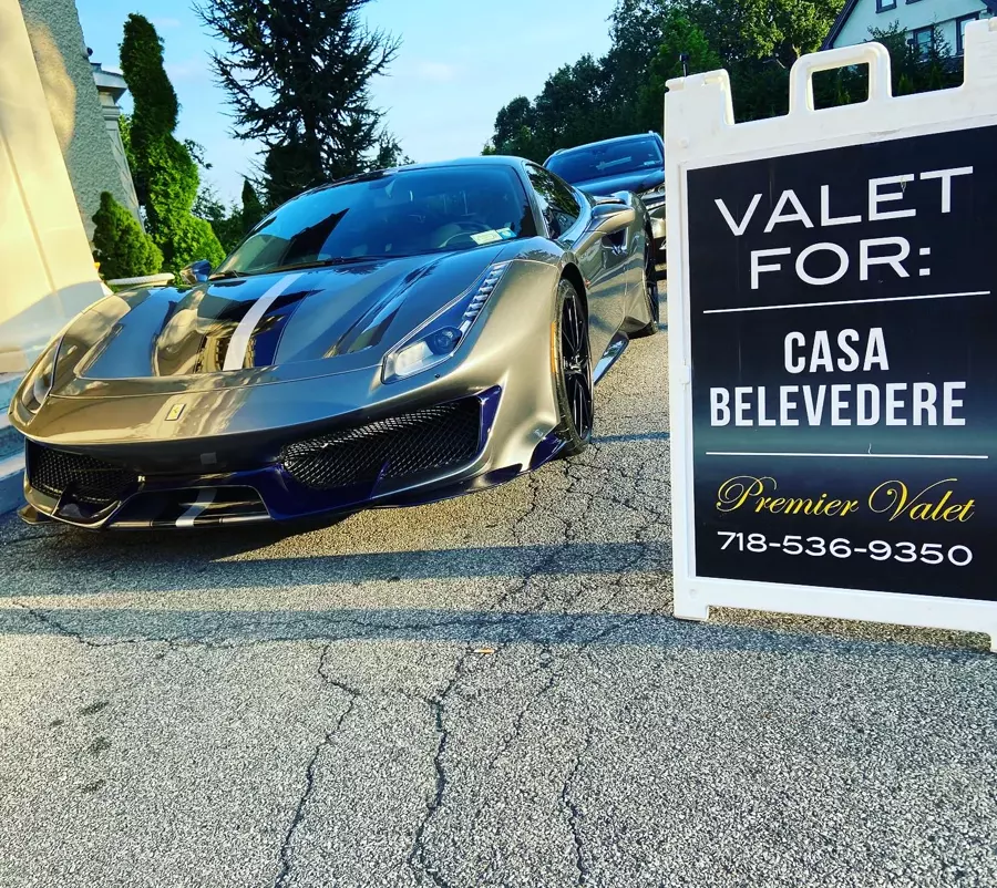 Gray Ferrari with racing stripes beside a Premier Valet sign for Casa Belvedere