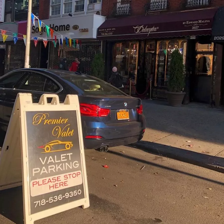 Premier Valet parking sign on the curb beside a blue BMW outside the Delacqua salon awning