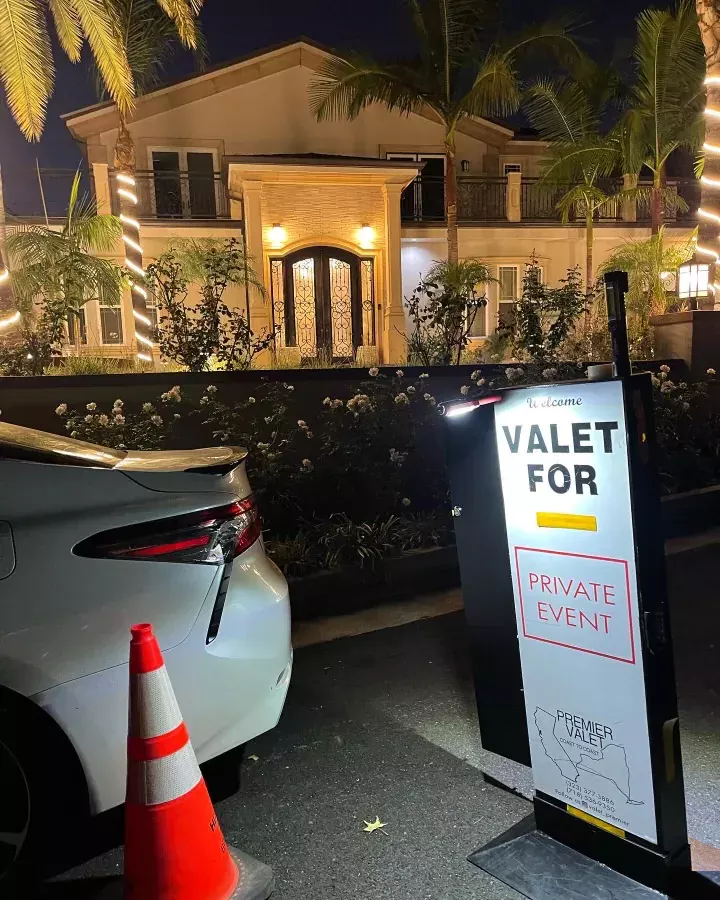 Lit Valet for Private Event sign by a white car and a cone outside a house with palm trees at night