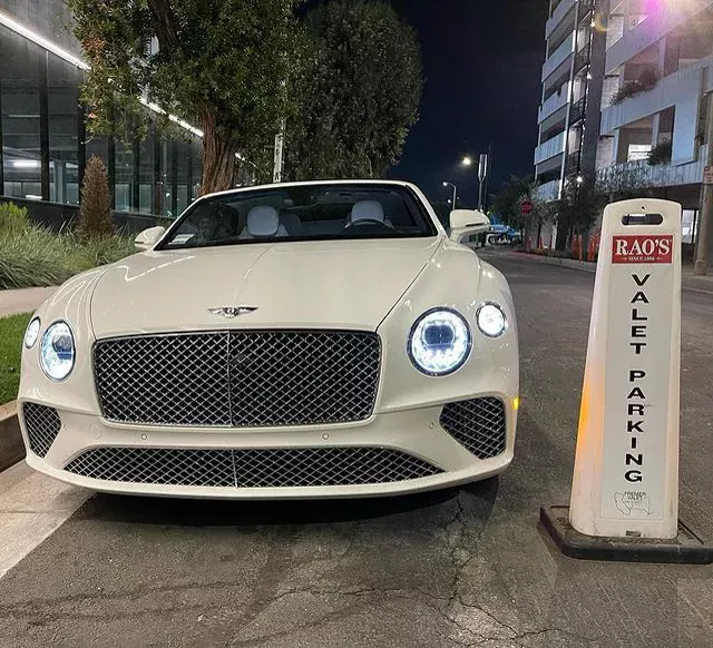 White Bentley convertible with the top down beside a Rao's valet parking cone at night