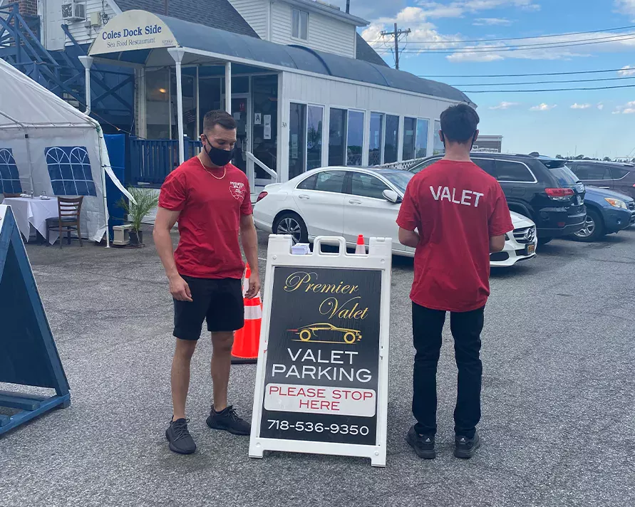 Two valet attendants in red shirts by a Premier Valet sign outside Coles Dock Side Sea Food Restaurant