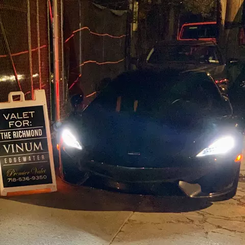 Black sports car with headlights on beside a valet sign listing The Richmond, Vinum and Edgewater