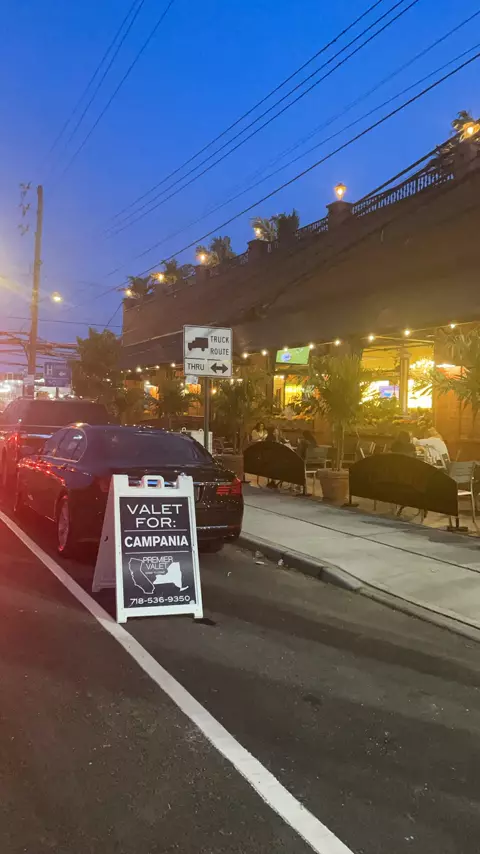 Premier Valet sign for Campania at dusk behind a black sedan, next to an outdoor dining area