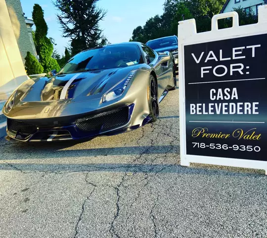 Gray Ferrari with racing stripes beside a Premier Valet sign for Casa Belvedere