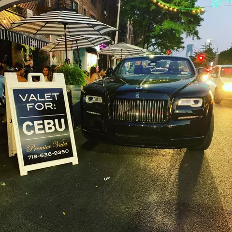 Black Rolls-Royce convertible beside a Premier Valet sign for Cebu at dusk, diners behind