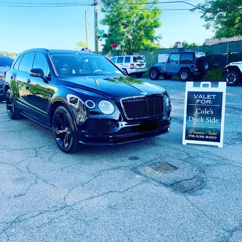 Black Bentley SUV in a parking lot beside a Premier Valet sign reading Valet For: Cole's Dock Side