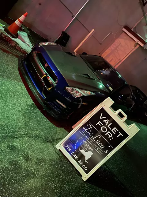 Blue Nissan GT-R at night behind a Premier Valet sign for DeLuca's Italian Restaurant