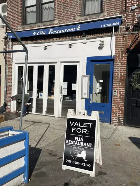Premier Valet sign reading Valet For: Eliá Restaurant on the sidewalk below Eliá Restaurant's blue awning