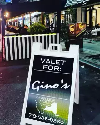Premier Valet sign reading Valet For: Gino's at night beside a striped outdoor dining enclosure
