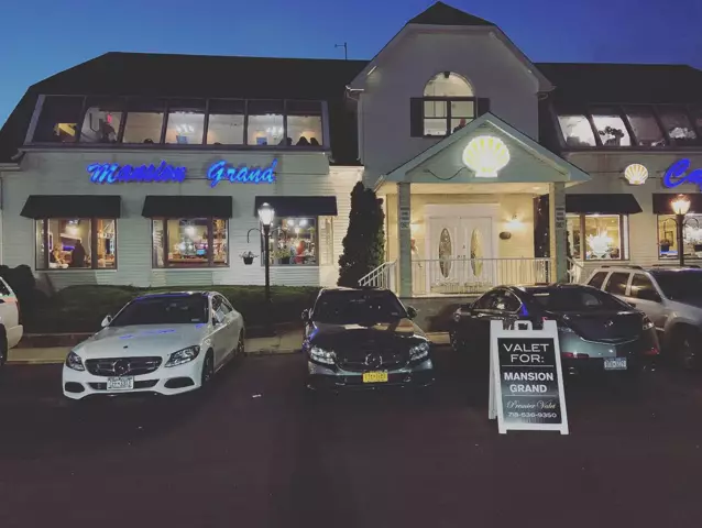 Mansion Grand building lit at dusk, with Mercedes sedans parked out front beside a Premier Valet sign