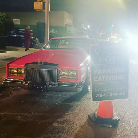 Red vintage Cadillac at night beside a sign on a traffic cone reading Valet For: Paradise Catering