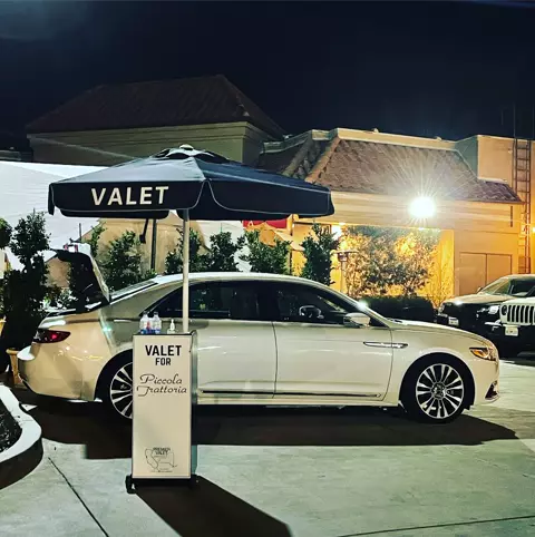 Valet podium for Piccola Trattoria under a navy VALET umbrella, beside a white sedan at night