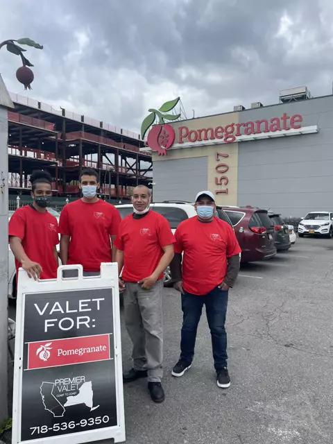 Four Premier Valet attendants in red shirts beside a Valet For: Pomegranate sign in a parking lot