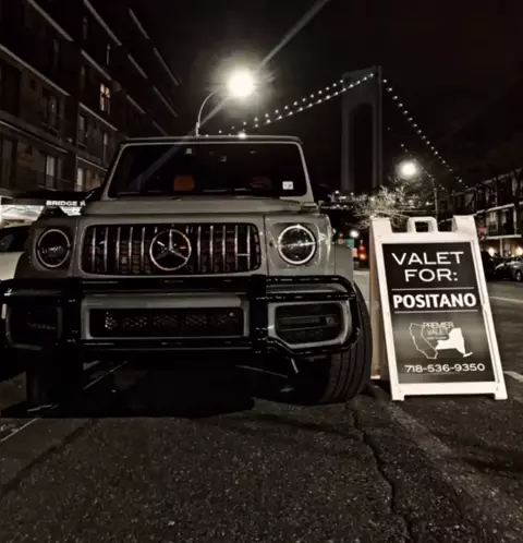 Mercedes G-Class parked at night beside a Valet For: Positano sign, with a lit suspension bridge behind