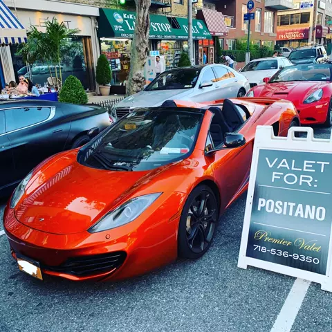 Orange McLaren convertible beside a Valet For: Positano sign, with a red Ferrari and other cars behind