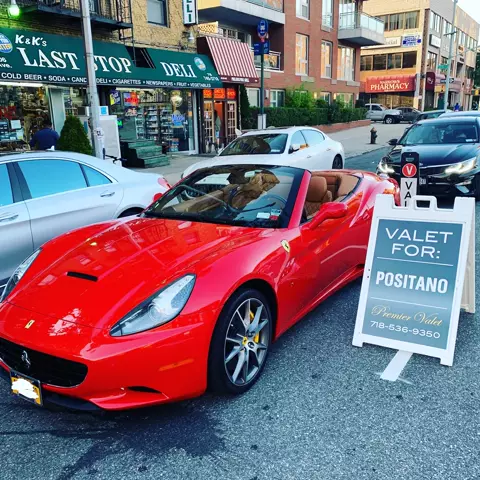 Red Ferrari convertible with tan interior parked beside a Valet For: Positano sign in front of a deli