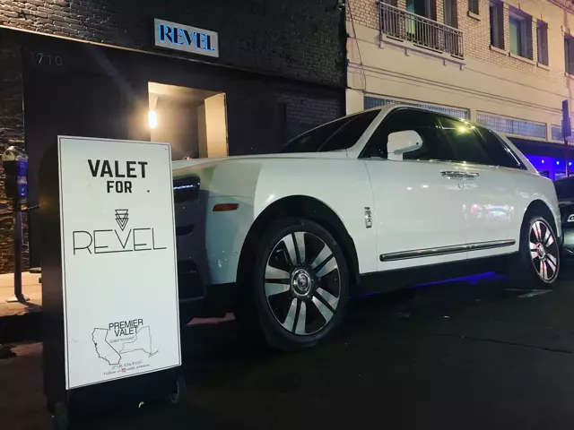 Valet for Revel sign beside a white SUV outside a building with a lit REVEL sign at night