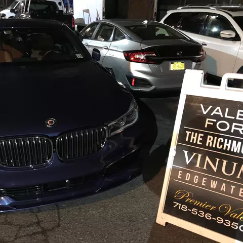 Dark blue BMW parked beside a partly cropped Premier Valet sign at night