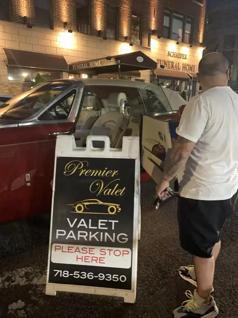 Man with keys by an open red Rolls-Royce and Premier Valet sign outside Schaefer Funeral Home at night