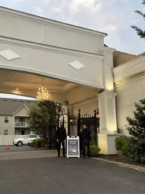 Two attendants in black beside a Premier Valet sign for Ariana's Grand under a chandelier-lit entrance