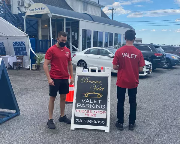 Two valet attendants in red shirts by a Premier Valet sign outside Coles Dock Side Sea Food Restaurant