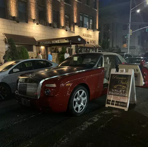 Red Rolls-Royce with an open door beside a Premier Valet sign outside Schaefer Funeral Home at night