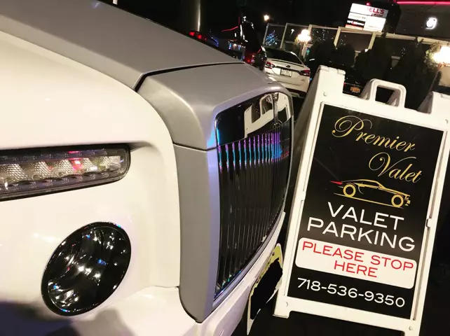 Front of a white Rolls-Royce beside a Premier Valet sign reading Valet Parking, Please Stop Here, at night