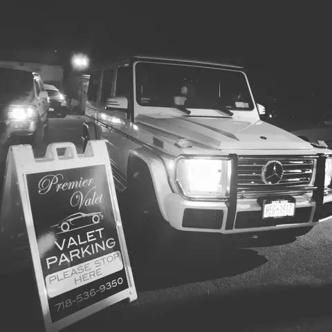 Mercedes-Benz G-Class with its headlights on beside a Premier Valet sign at night